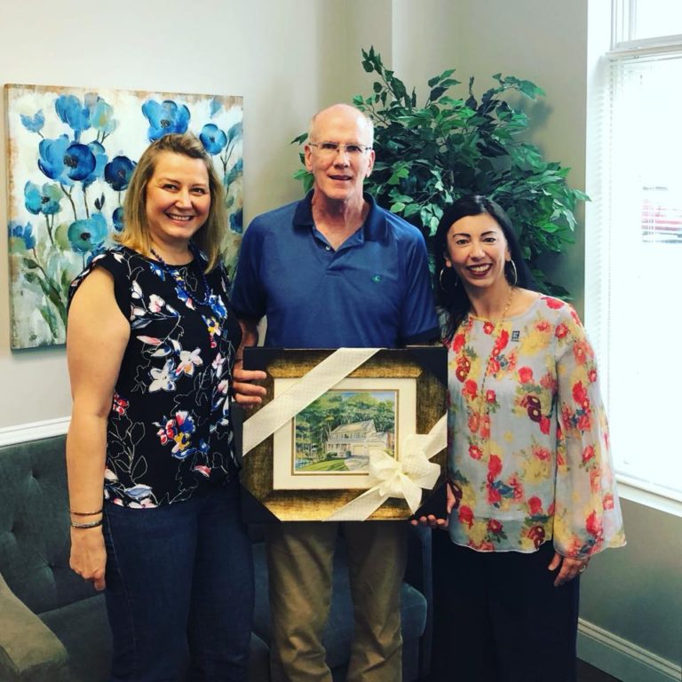 A man and two women holding a picture frame.